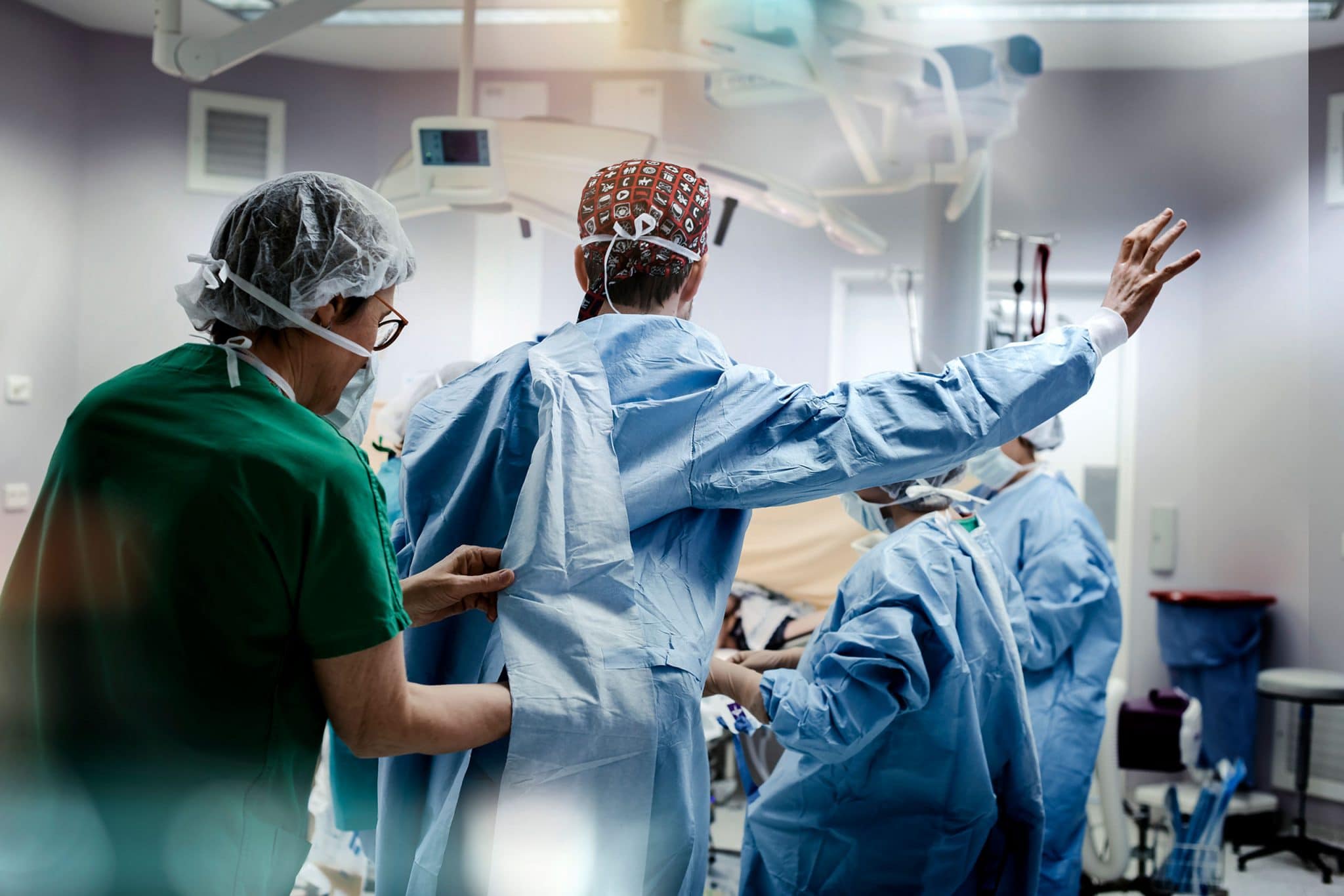 reportage photo sur les professionnels de la santé en milieu hospitalier pour la Haute Autorité de Santé. Une aide soignante habille le chirurgien obstétricien avant une césarienne