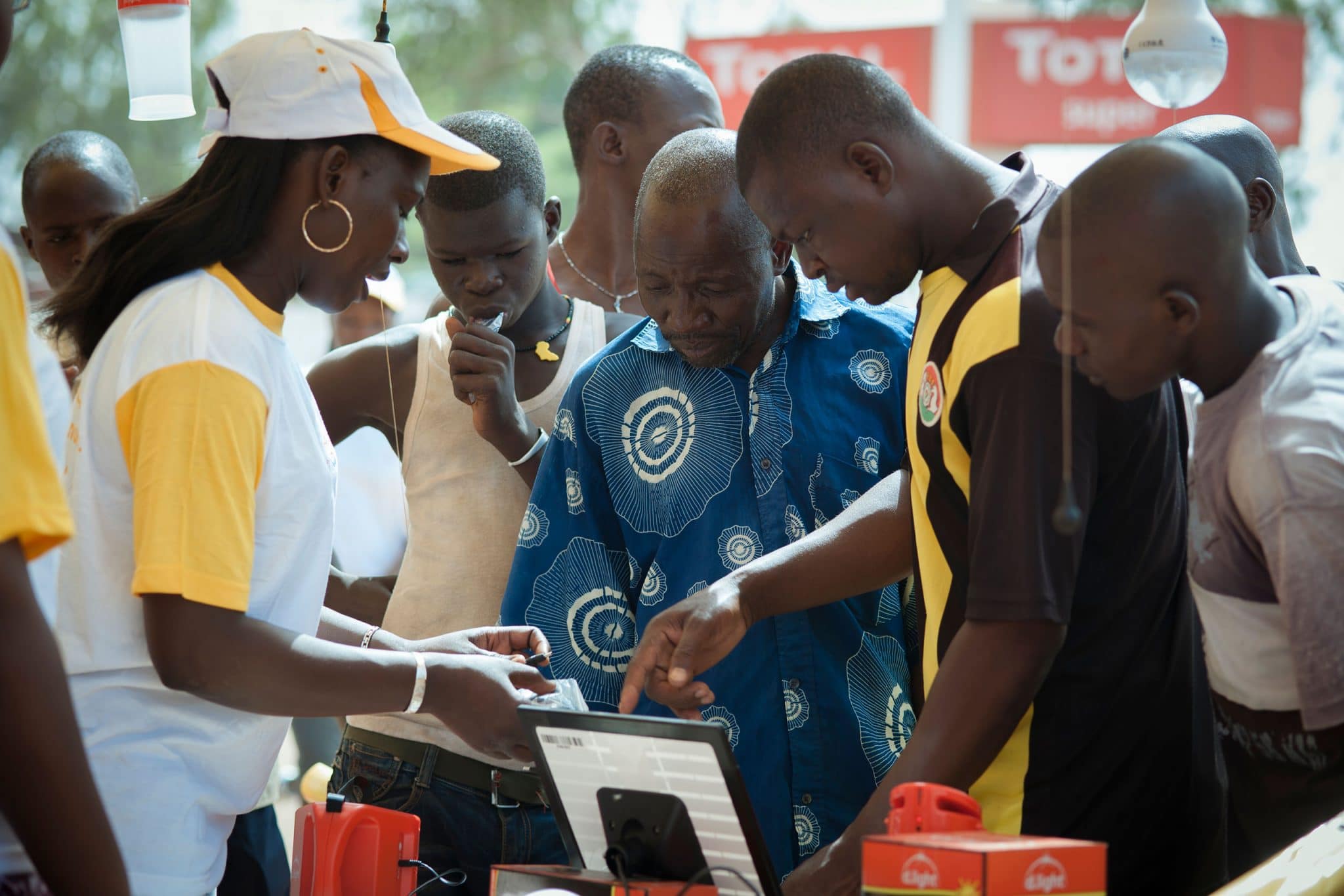 des passants s'interessent aux lampes solaire Awango By TotalEnergies dans une station service