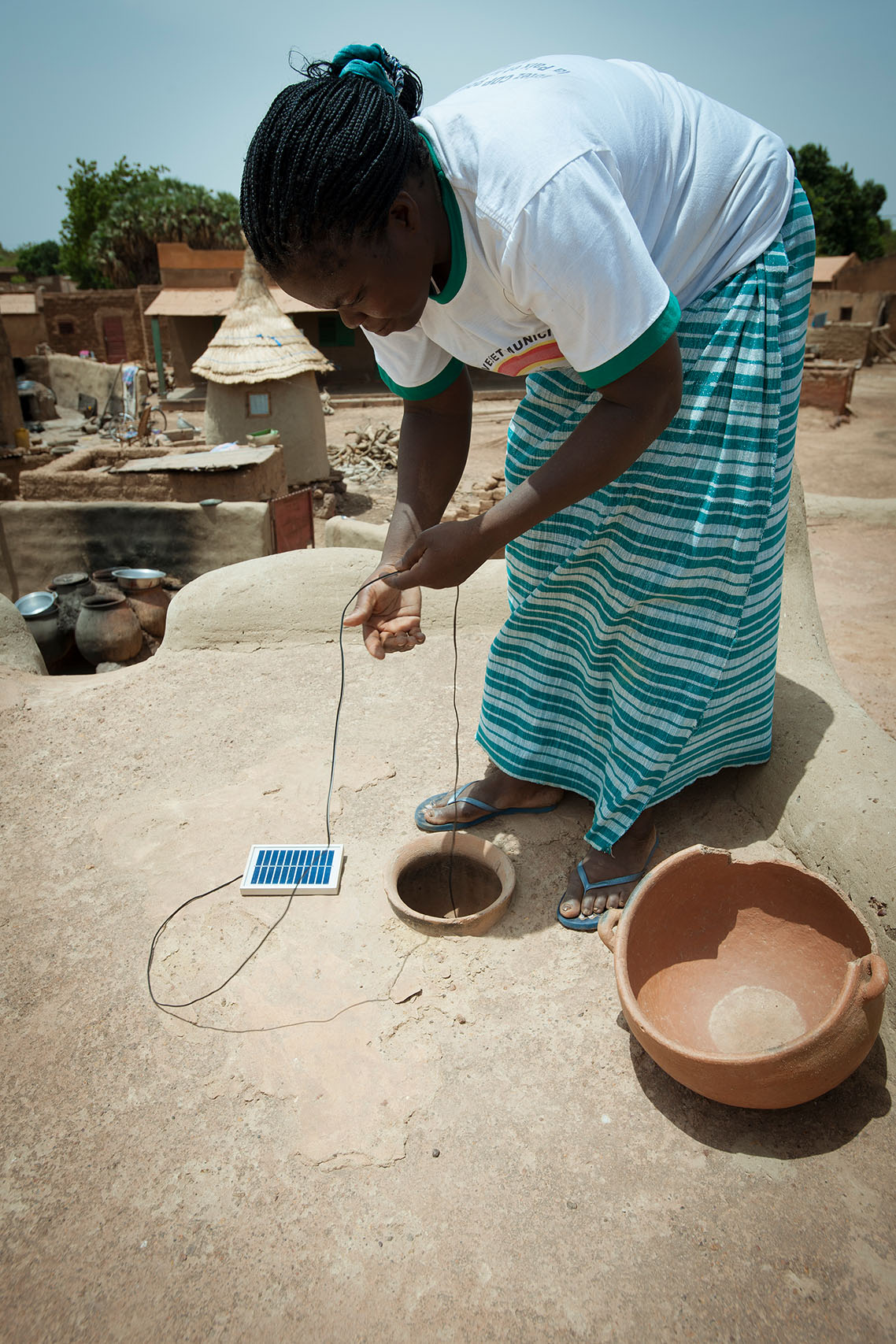 A Réo, à 120km de Ouagadougou, Jeanne KANYALA dont la maison n'est pas reliée au reseau électrique fait passer le cable d'alimentation de sa lampe Awango By TotalEnergies par une ouverture dans son toit. Le panneau solaire peut rester en place de façon définitive.