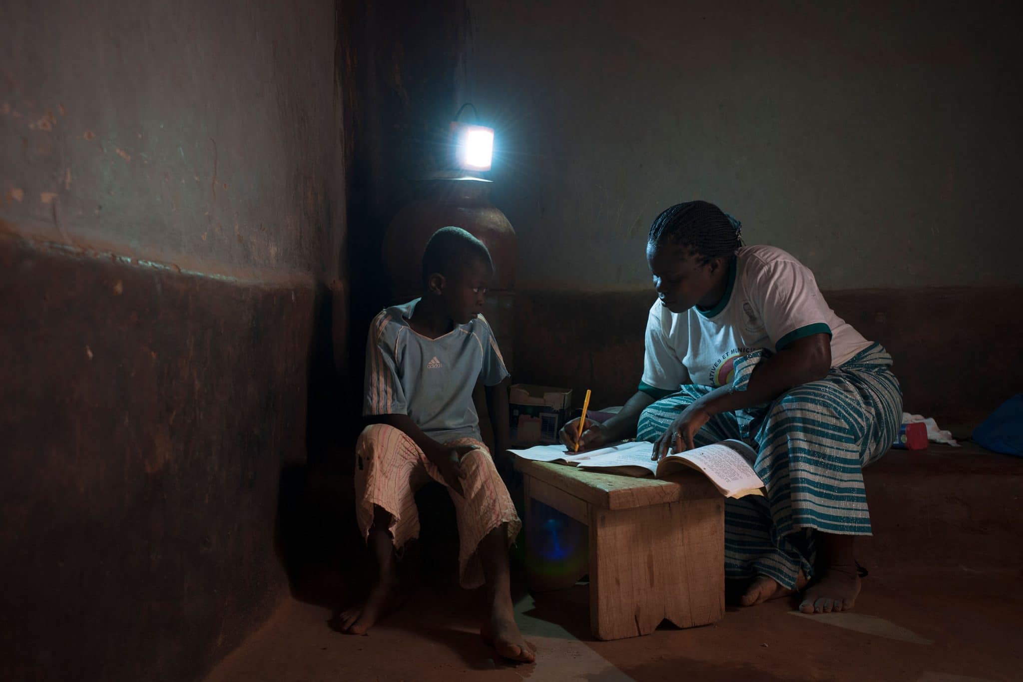 Au Burkina Faso, une maman aide son fils à faire ses devoirs dans sa case grace à son éclairage solaire Awango by TotalEnergies