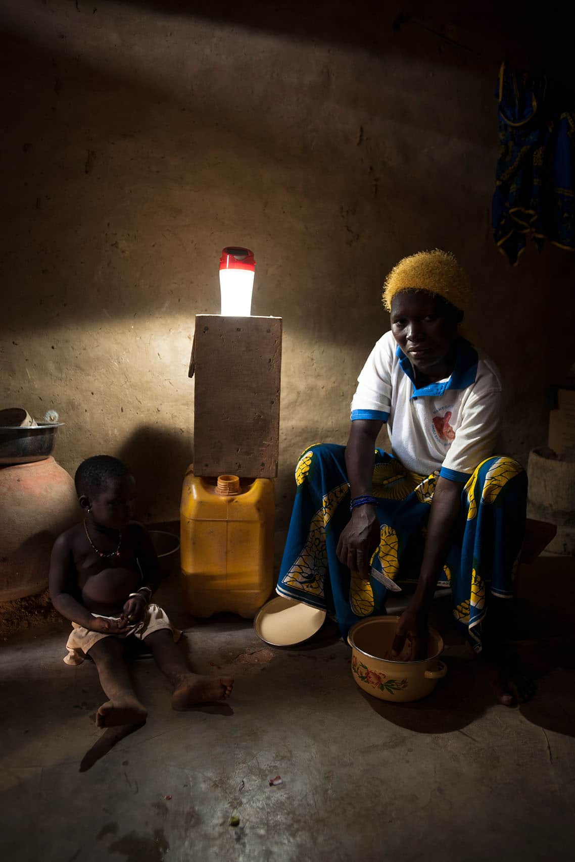 Une femme prépare le dîner dans sa case à Ouagadougou grace à la lumière de son éclairage solaire Awango by TotalEnergies