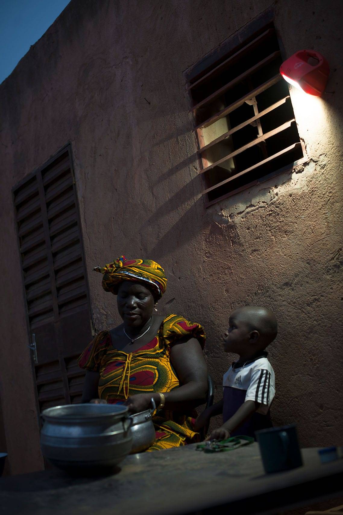 Femme à Ouagadougou préparant le repas sous l'éclairage d'une lampe à énergie solaire Awango by TotalEnergies