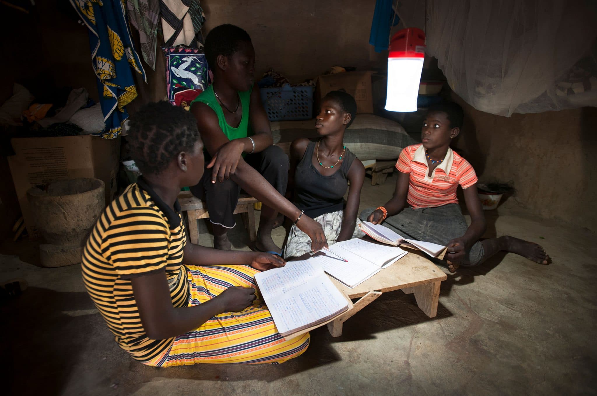 des enfants font leurs devoirs scolaires dans une case des faubourgs de Ouagadougou grace aux lampes solaire Awango by TotalEnergies