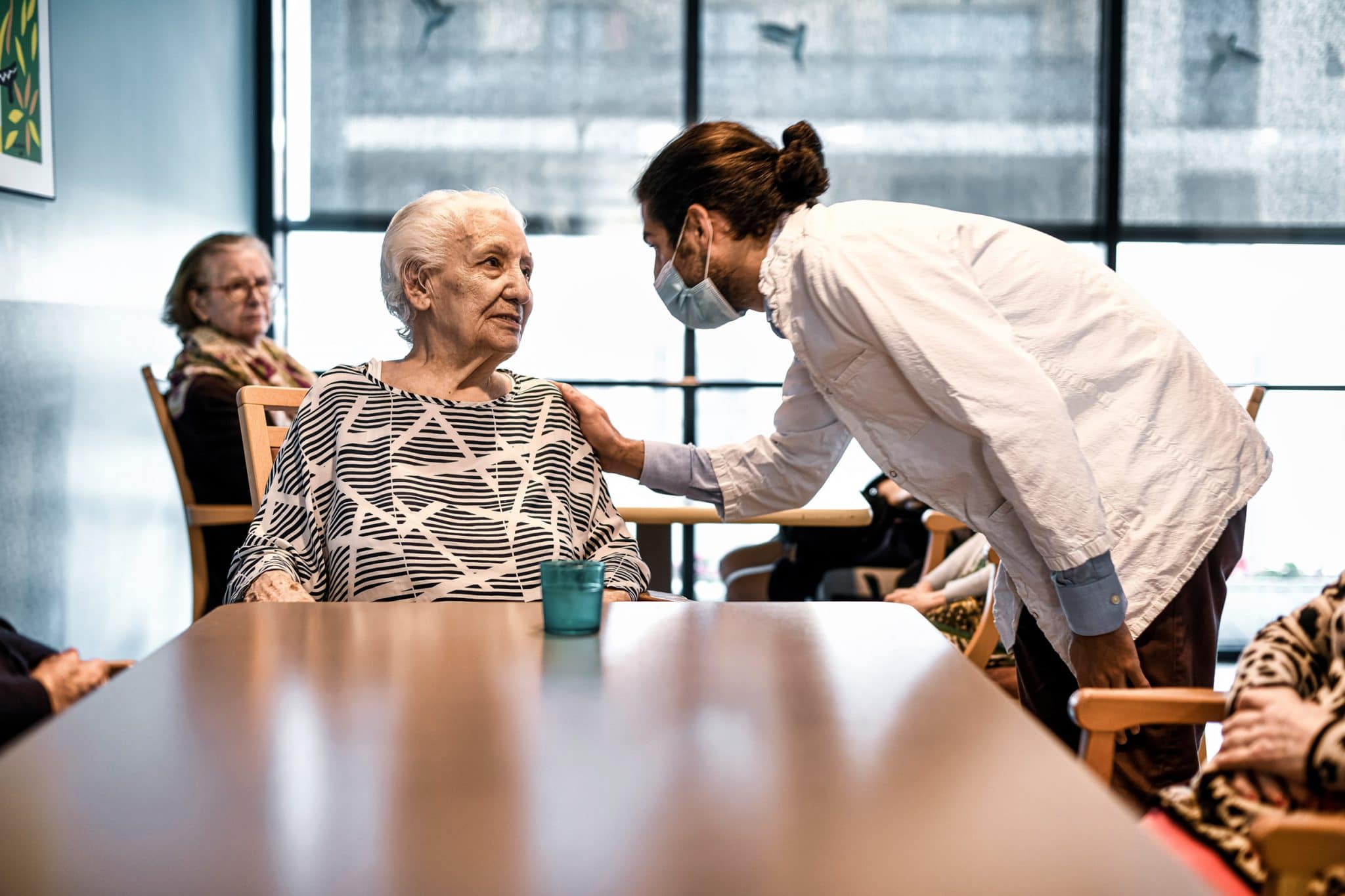 EHPAD Lasserre. Geste affectueux d'un kinésithérapeute avec une résidente. Photographe santé.